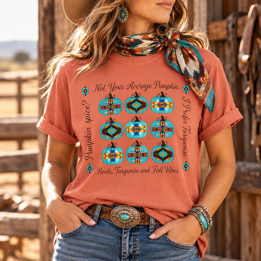 A woman wearing a terracotta short-sleeve graphic T-shirt with a turquoise, black, and orange pumpkin design and text reading 'Not Your Average Pumpkin' and 'Pumpkin Spice! Boots, Turquoise and Fall Vibes.' She is also wearing a patterned turquoise neck scarf, blue jeans, a western belt, and bracelets, photographed outdoors in front of a rustic wooden fence.