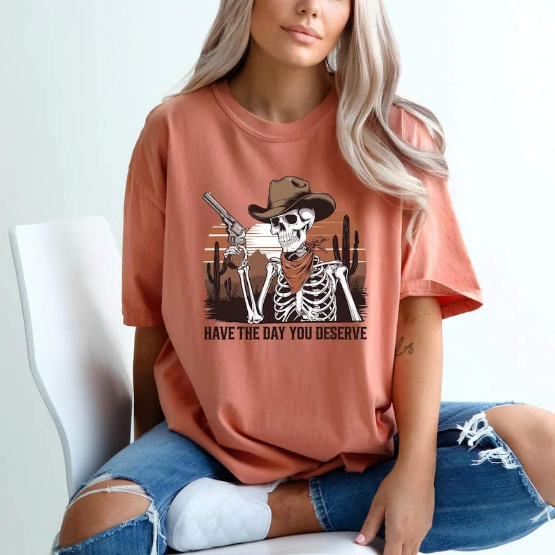 Graphic tee on model with picture of skeleton holding a gun and the quote have the day you deserve