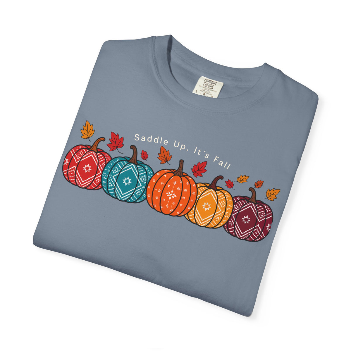 A folded slate blue crewneck t-shirt featuring a graphic of four patterned pumpkins in red, teal, orange, and burgundy with scattered autumn leaves and the text 'Saddle Up, It's Fall'.
