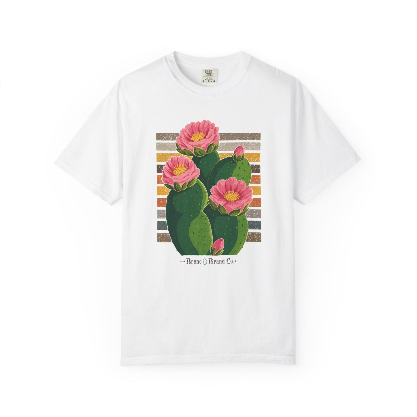 A white short-sleeve crewneck t-shirt featuring a graphic print of a green prickly pear cactus with three pink flowers blooming from the side, set against a striped background with the text 'Pica Brasa Brand Co.' printed below.