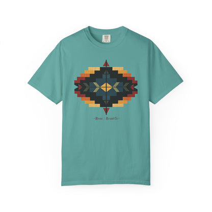 A teal short-sleeve crewneck t-shirt featuring a central geometric design in a Southwestern style with yellow, orange, red, and black colors. Below the graphic, the text 'Bronc & Brand Co' is printed in a stylized font.