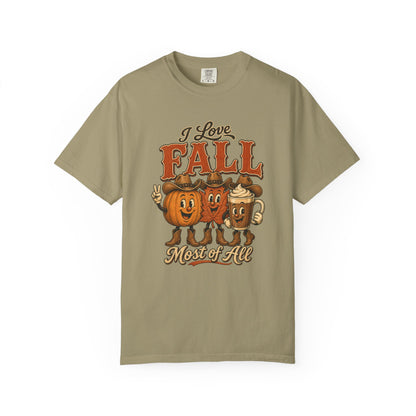 A sage green crewneck t-shirt featuring a retro-style graphic that reads 'I Love FALL Most of All' above three cartoon characters representing pumpkin, hot dog, and mug foods, displayed on a clean white background.