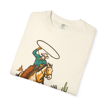 An off-white folded t-shirt with a vintage-style western graphic of a cowboy on a horse swinging a lasso, displayed on a clean white background.