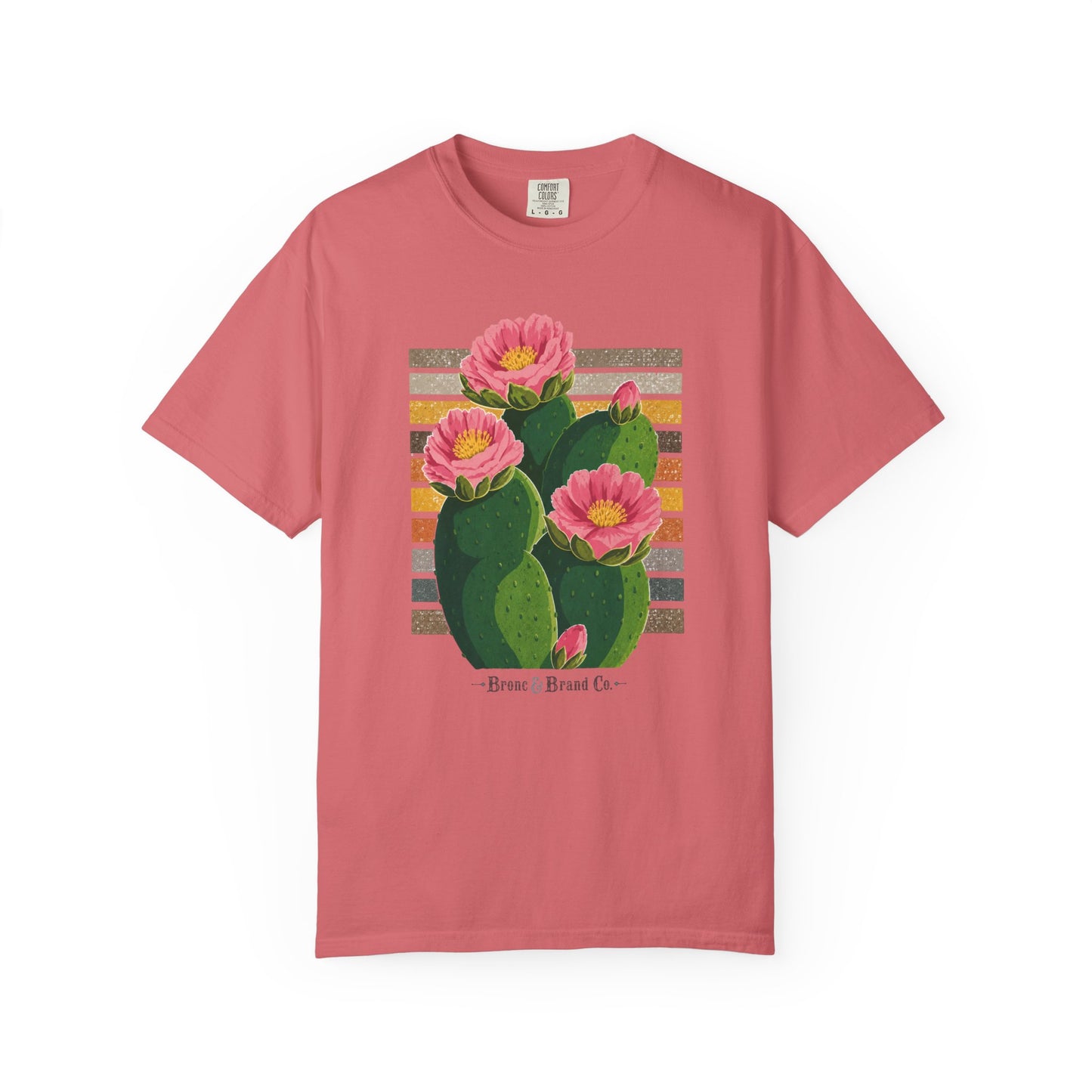 A dusty rose pink short-sleeve t-shirt with a graphic print of a green prickly pear cactus with three pink flowers blooming from it, set against a striped background. The text 'Bust a Brad Co.