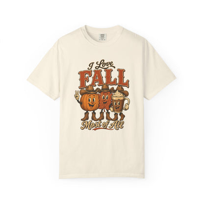 An off-white short-sleeve t-shirt with a vintage-style autumn graphic on the front. The graphic features three cartoon pumpkins wearing cowboy hats, with the text 'I Love FALL Most of All' written above and below them.