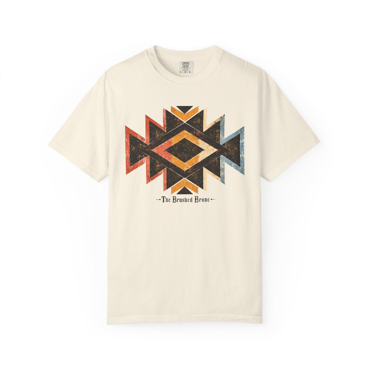 An off-white short-sleeve t-shirt featuring a distressed geometric Southwestern-style diamond pattern in black, orange, and red on the chest, with the text '-The Brushed Bronc-' printed below.