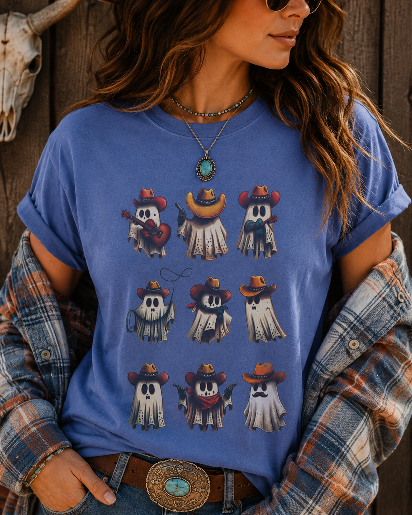 A woman wearing a blue graphic t-shirt with a 3x3 grid of cute cartoon ghosts in cowboy hats, styled with a plaid shirt draped off her shoulders and a rustic wooden background.