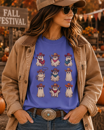 A woman wearing a blue graphic t-shirt with a 3x3 grid of cute cartoon ghosts in cowboy hats, styled with a tan jacket, jeans, and a brown cap in an outdoor fall festival setting.