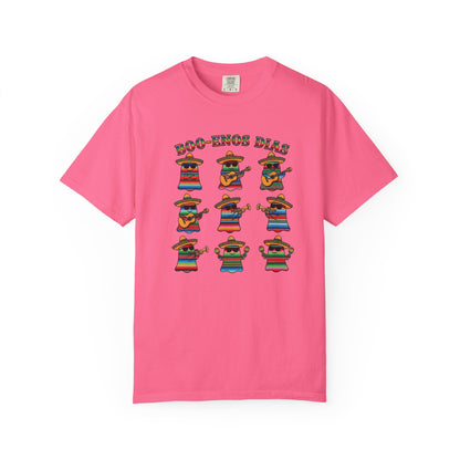 A pink short-sleeve crewneck t-shirt featuring a graphic print of nine cartoon mariachi musicians wearing colorful ponchos and sombrero hats, with the text 'ECO-ZONOS DIAS' above them.