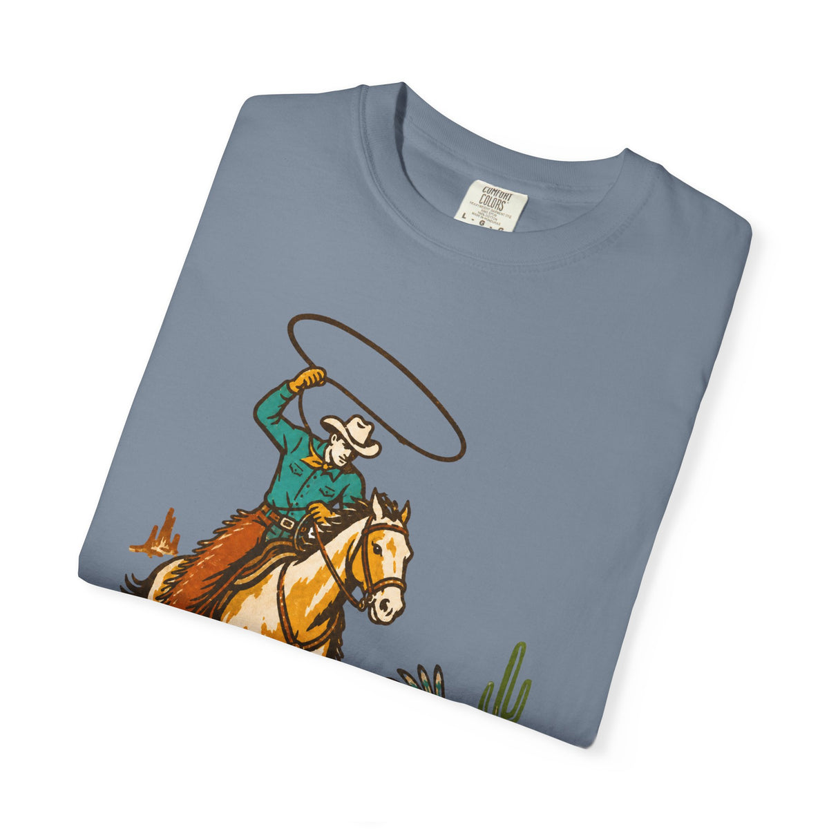 A folded slate blue crewneck t-shirt featuring a western graphic of a cowboy on a horse swinging a lasso, displayed on a clean white background.