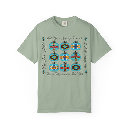 A sage green short-sleeve t-shirt with a graphic print of nine colorful patterned pumpkins and text reading 'Not Your Average Pumpkin' and 'Pumpkin Spice Boots, Taqueria and Fall Vibes' on a white background.