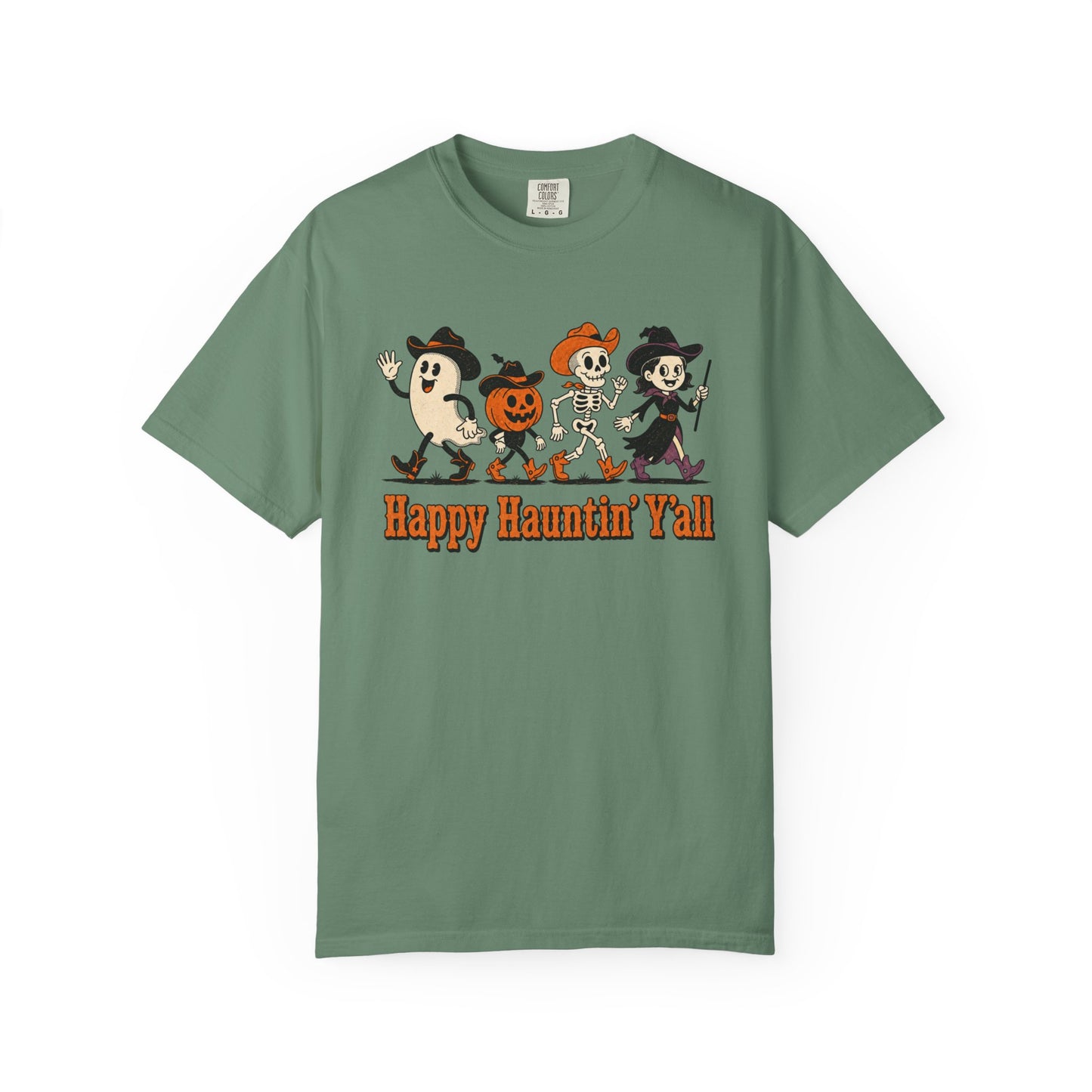 A sage green short-sleeve t-shirt with a cartoon graphic of four Halloween characters (a ghost, a pumpkin-headed character, a skeleton, and a witch) and the text 'Happy Haunting' Y'all' printed on the front.