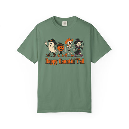 A sage green short-sleeve t-shirt with a cartoon graphic of four Halloween characters (a ghost, a pumpkin-headed character, a skeleton, and a witch) and the text 'Happy Haunting' Y'all' printed on the front.
