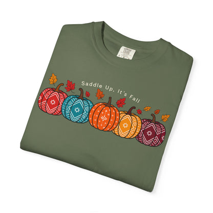 A folded brown crewneck t-shirt featuring a graphic of five patterned pumpkins in red, blue, orange, and purple, with small autumn leaves and the text 'Saddle Up, It's Fall' printed on the chest.