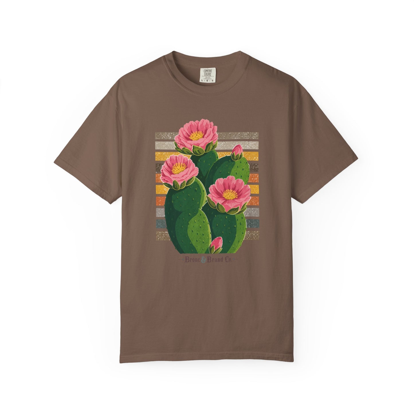 A brown short-sleeve crewneck t-shirt featuring a graphic print of a green prickly pear cactus with three pink flowers and yellow centers, set against a striped background.
