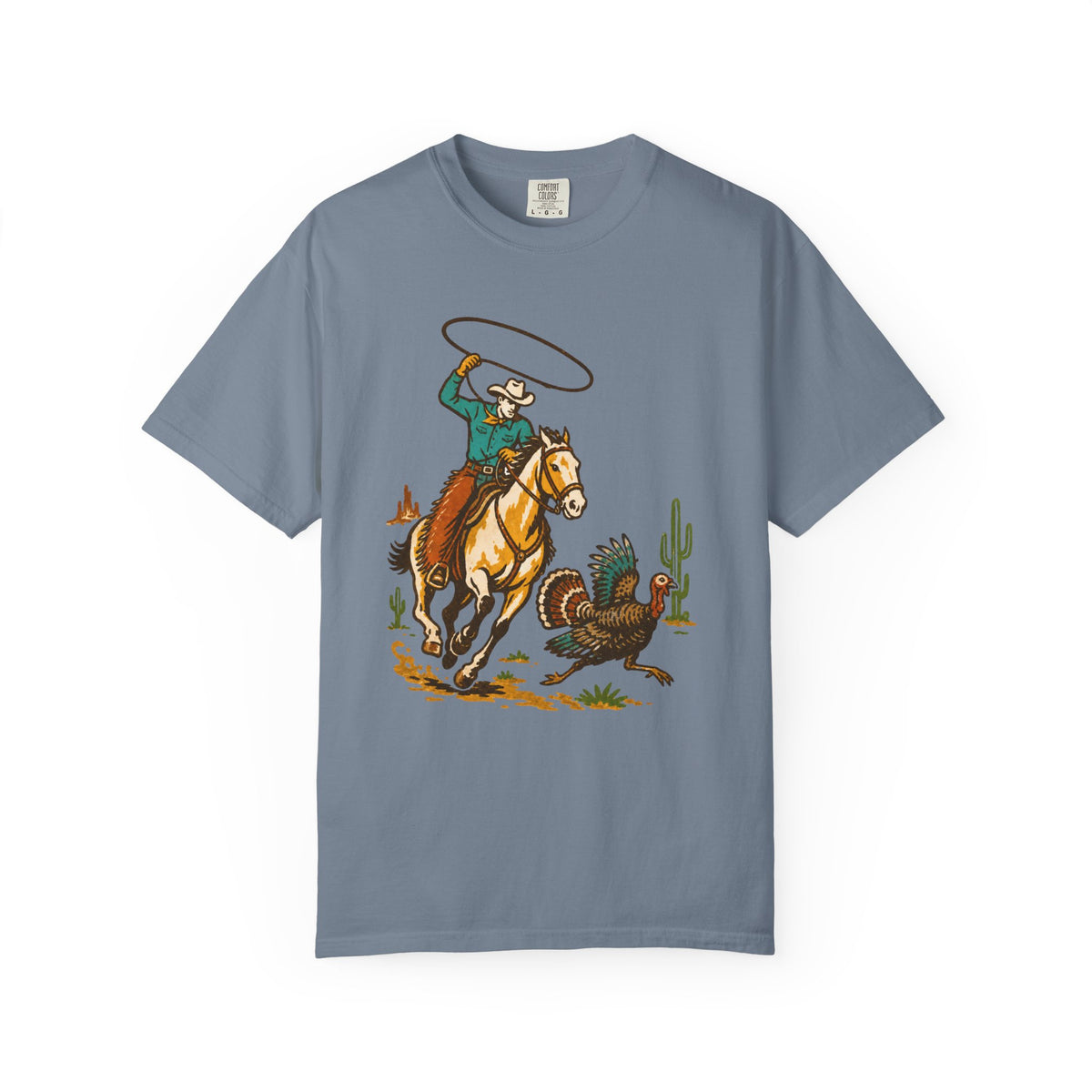 A slate blue crewneck t-shirt featuring a colorful graphic print of a cowboy riding a horse and lassoing a turkey, displayed on a clean white background.