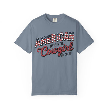 American by Birth Cowgirl by Choice tee with patriotic western lettering laid flat against white background in blue jean color