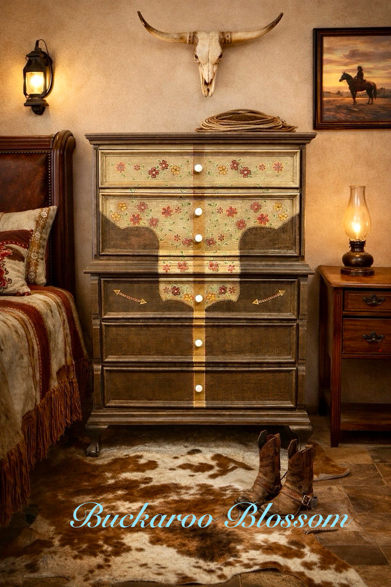 Hand-painted western dresser named Buckaroo Blossom featuring a shirt yoke design with floral details and pearl snap knobs, styled in a rustic bedroom with cowhide rug, cowboy boots, and warm western décor.