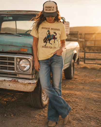 Person wearing a bronc and brand co t-shirt with a graphic design, standing next to an old truck in a rural setting.
